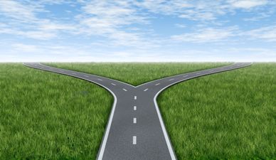 Cross roads horizon with grass and blue sky showing a  fork in the road or highway business metaphor representing the concept of a strategic dilemma choosing the right direction to go when facing two equal or similar options.