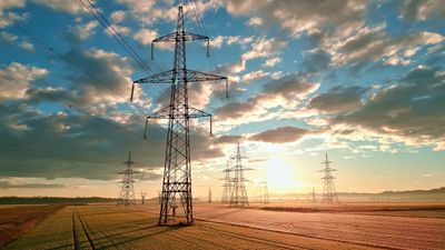 Power lines stretch across a vast field, symbolizing energy's omnipresence and connectivity. The sunset casts a warm glow, highlighting the balance between nature and technology.