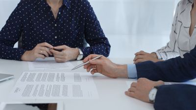Business people reviewing contract during a meeting, pointing at specific clauses and discussing potential amendments before signing the agreement.