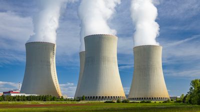 Nuclear power plant cooling towers releasing steam into a blue sky, representing energy production