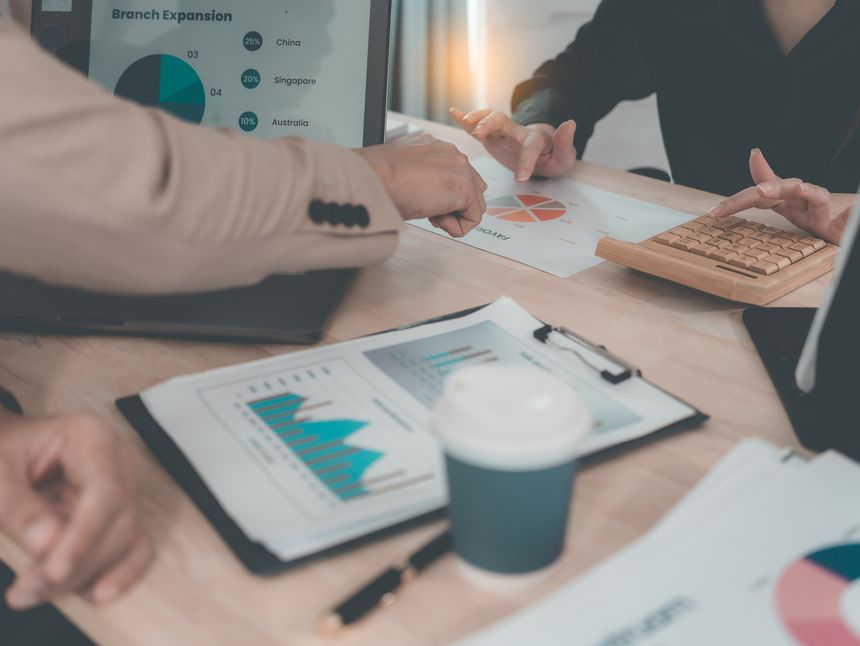A statistician is preparing charts and documents for a meeting. A team of professionals is reviewing financial documents. Pointing to charts on the desk. Working.