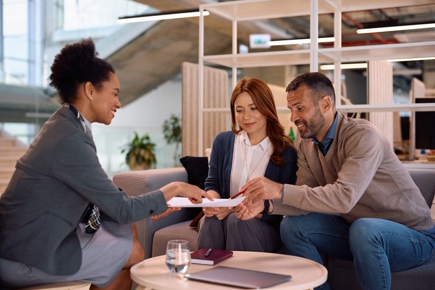 Happy couple and their financial advisor going through terms of a contract before signing it in the office.