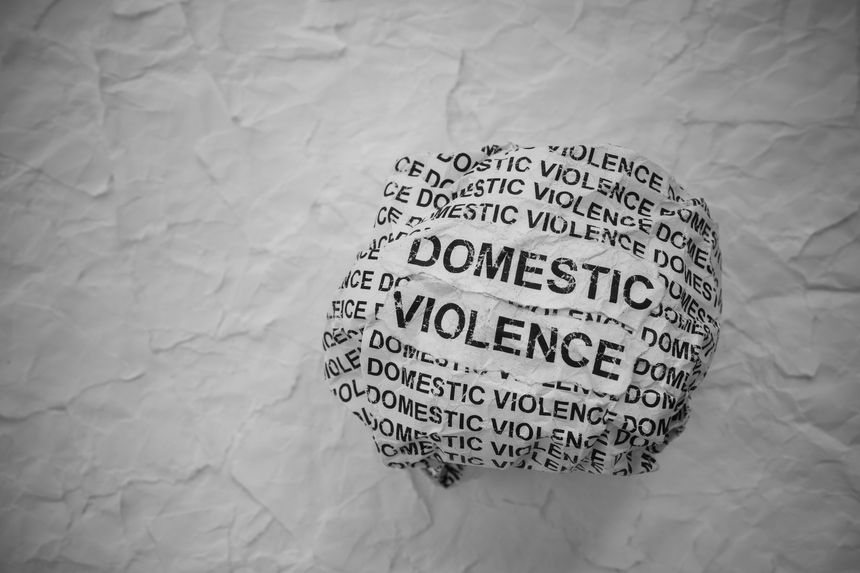 Crumpled paper ball with words Domestic Violence on torn white paper pieces background.