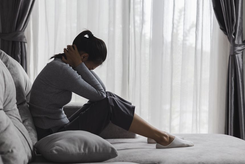 Sad and depressed woman sitting on sofa at home. Suicide due to depression.