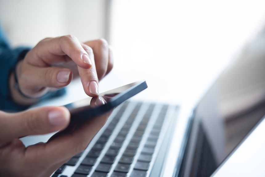 Woman using mobile phone with laptop computer on office table. Business woman surfing the internet, searching the information on smartphone working on laptop computer at workplace