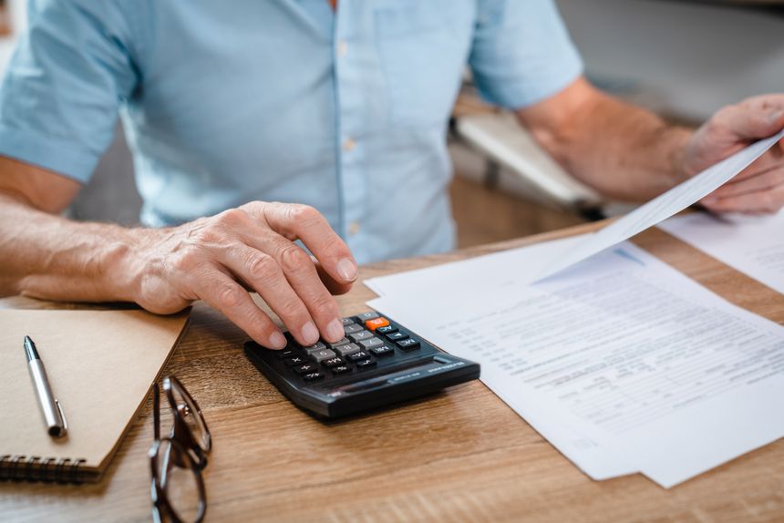Close up of senior successful businessman and investor working on paper work in the office, mature gray haired male boss working with contracts and accounts financier using laptop at work.