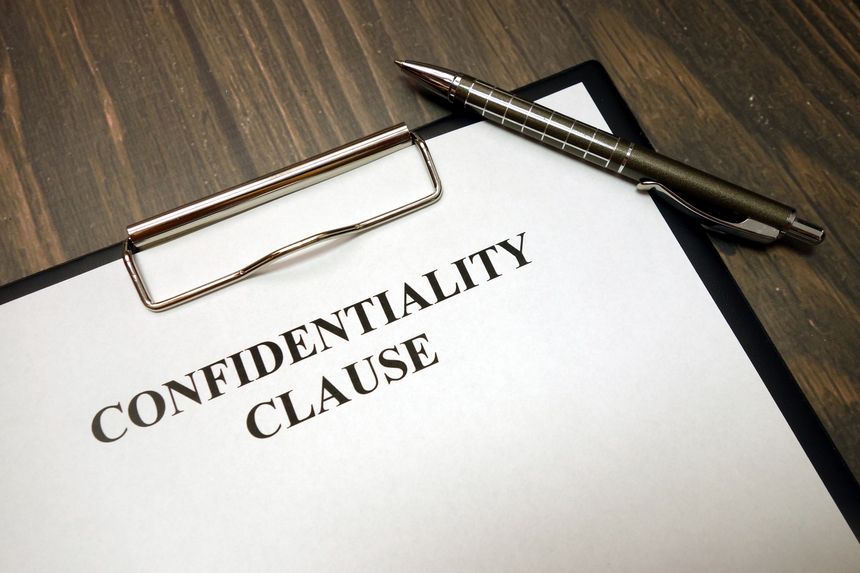 Clipboard with confidentiality clause and pen on wooden desk background