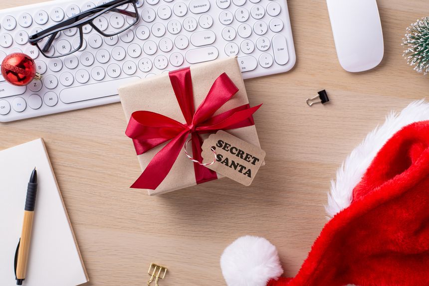Christmas-themed office desk featuring a wrapped present with a red bow, keyboard, Santa hat, and decorative items, symbolizing holiday spirit and workplace celebration