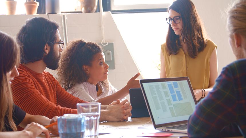 Multi-Cultural Business Team Meeting Around Table In Office With Laptop And Documents
