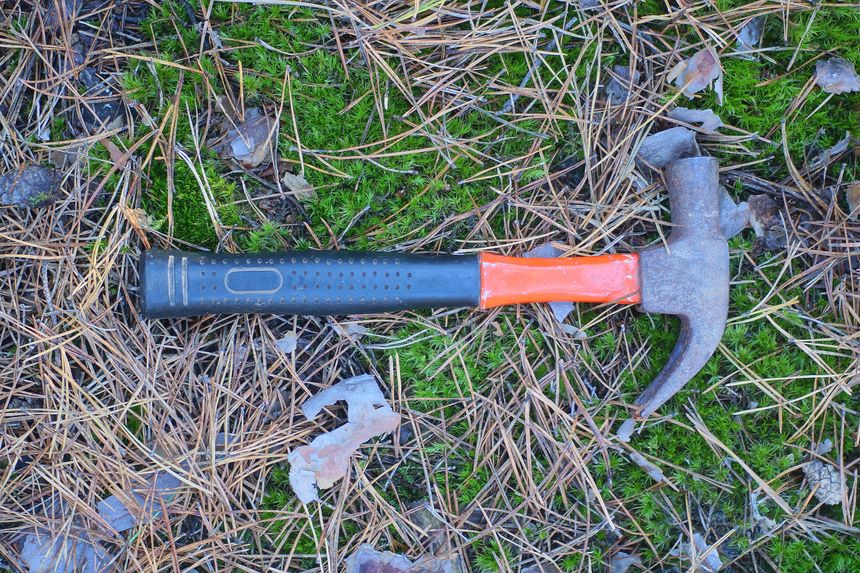 one brown rusty iron hammer with a red and black handle lies on the ground and green moss in the summer forest