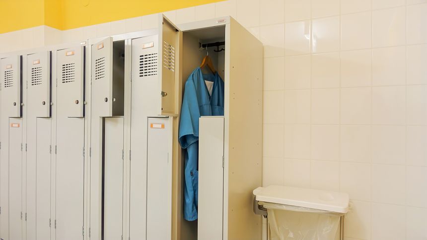 Open metal lockers in the staff locker room. In one of them, a nurse's clothes are hanging on a hanger - one turquoise smocks and white trousers. Concept of acute shortage of nursing staff and doctors in hospitals and nursing homes.