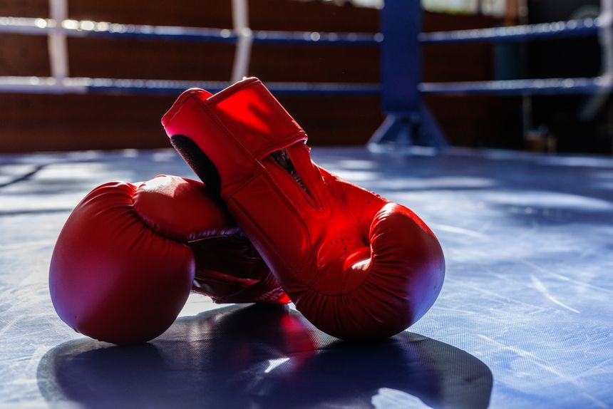 Bright red boxing gloves on a gym ring mat with bold shadows, ideal for training, competition, fitness and combat sport themes.