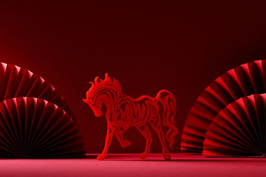 Red horse silhouette zodiac symbol centered between traditional paper fans on a red background. Chinese New Year 2026 concept.