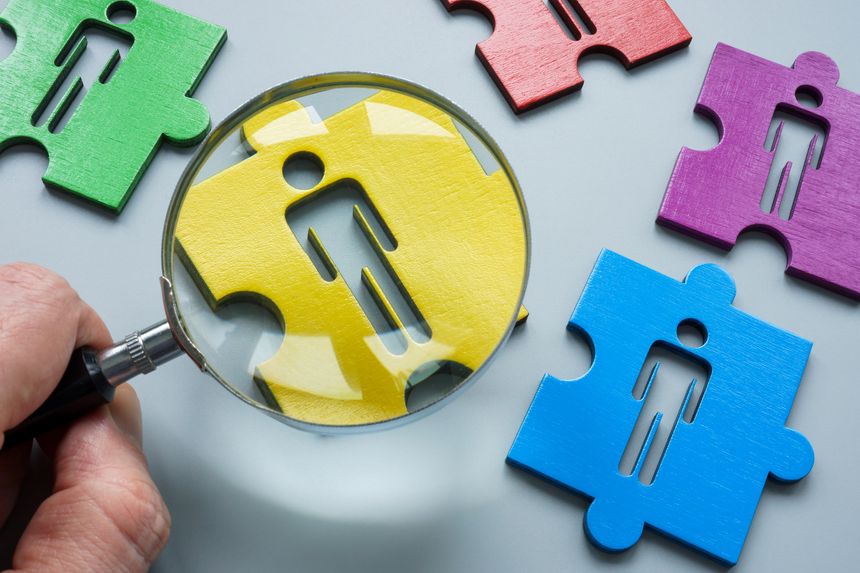 Talent search concept. A hand with magnifying glass and a puzzle with a figurine of a team candidate.