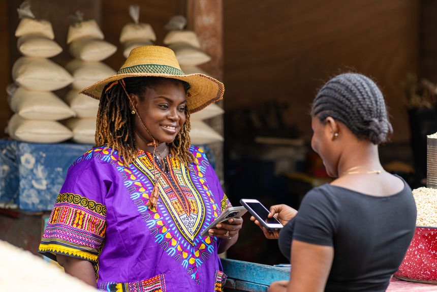 African local market woman accepts mobile money payment from a customer at her vibrant outdoor stall. Small business owner, SME.