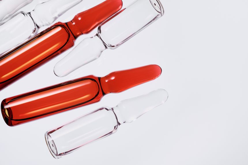 Glass ampoules containing red liquid and clear liquid on a clean white surface