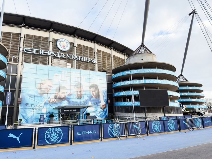 Manchester, UK - November 16, 2025: A modern stadium exterior with blue branding, banners, and distinctive circular towers at Manchester City Stadium.