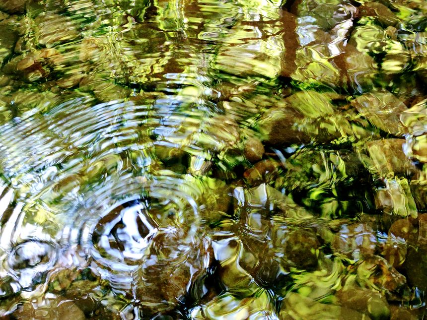 Abstract flowing water colourful swirling patterns, and blue sky reflection, South Wales UK.
