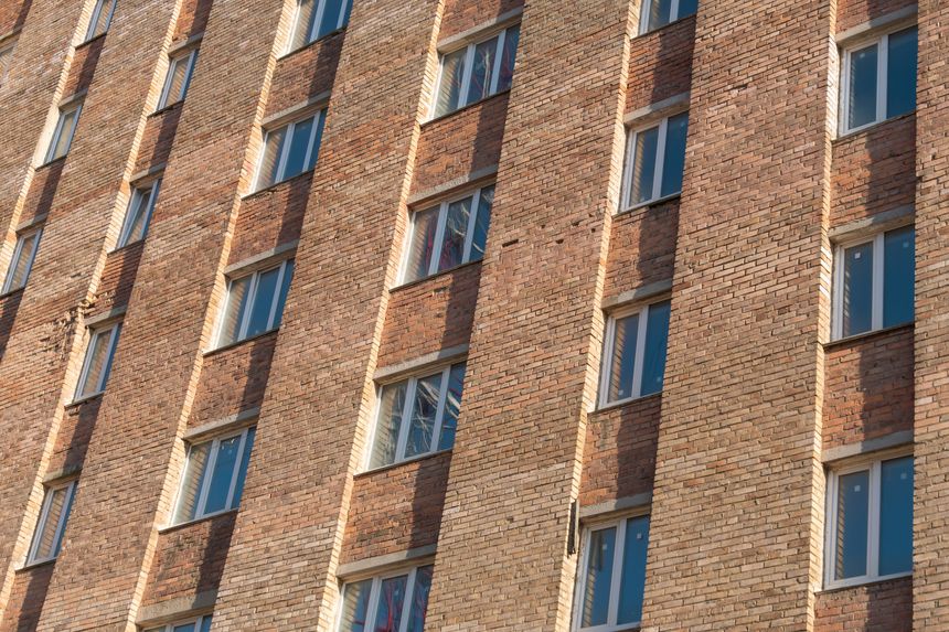 Brick building exterior features numerous windows and a textured facade, set against a clear blue sky, highlighting modern architectural elements