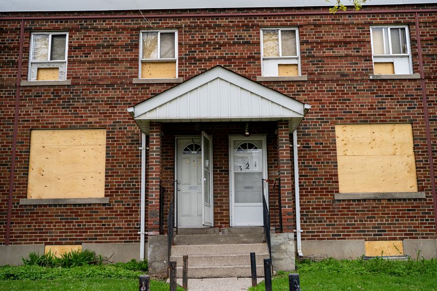 Boarded up windows on abandoned residential building facade with brick exterior.