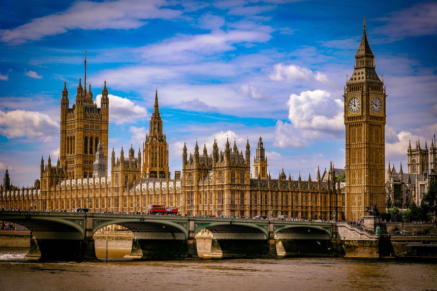 Iconic view of the Palace of Westminster and the Elizabeth Tower, commonly known as Big Ben, in London, England. The Gothic Revival architecture is seen from across the River Thames, with Westminster Bridge in the foreground and a red double-decker bus crossing. A world-famous landmark symbolizing British democracy, heritage, and culture, and one of the most visited attractions in the United Kingdom.