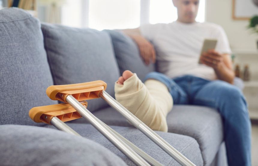 Close up shot of a man broken and bandaged leg resting on a sofa at home, with crutches nearby. He is in the process of rehabilitation after a trauma or injury, focusing on recovery.
