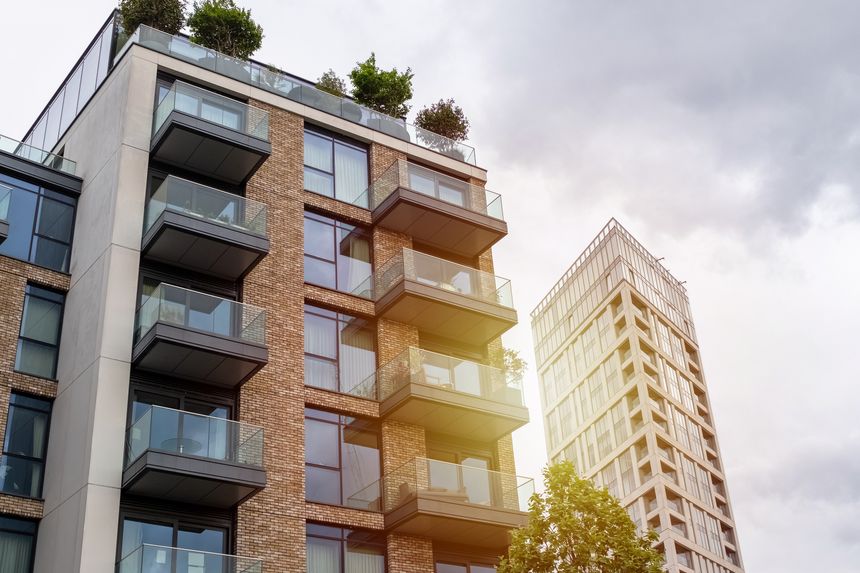 Modern apartments with spacious balconies and rooftop gardens under a cloudy sky, emphasizing green living.