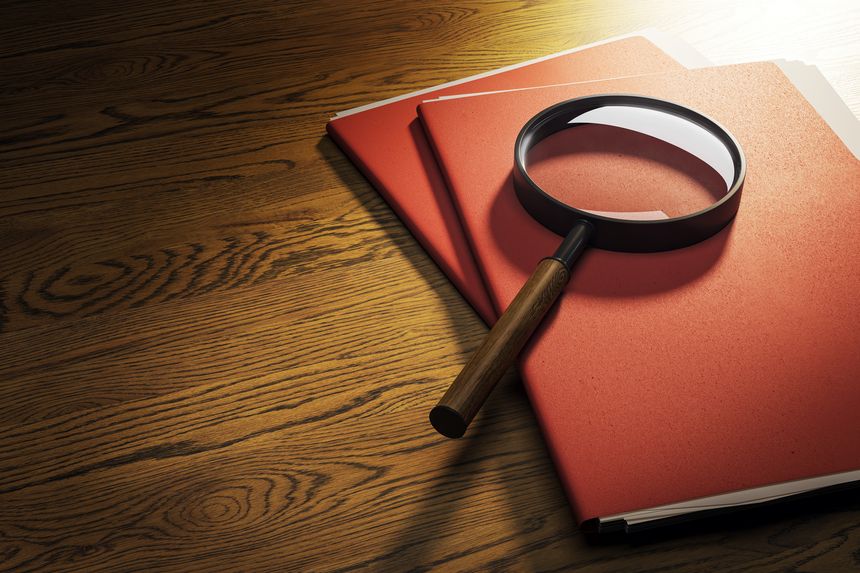 Red file folders with magnifying glass on dark wooden desktop under spotlight, top view, symbolizing investigation, research or business analysis. 3D Rendering