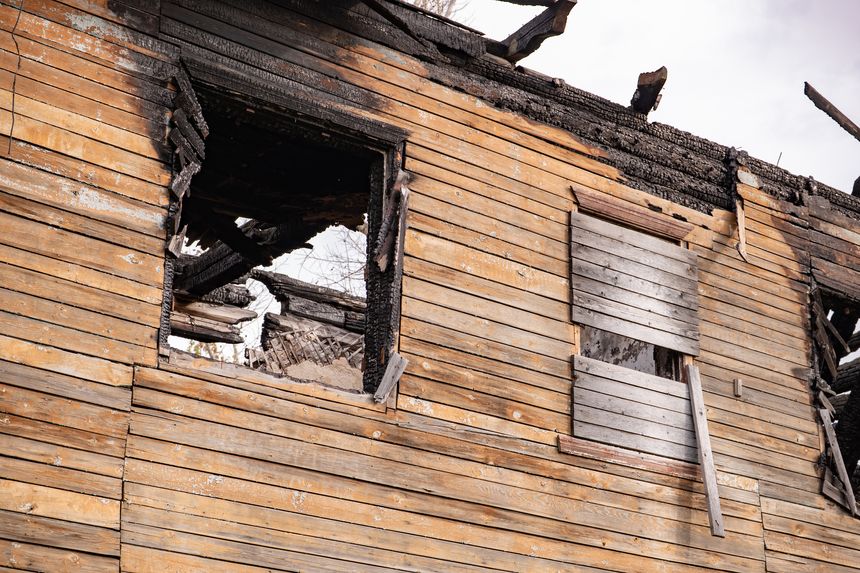 Destroyed wooden house facade showing fire damage and structural collapse after disaster