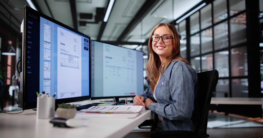 Professional Woman Analyzing Invoices On Computer Screen For Financial Audit