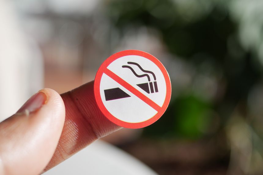 A person is holding a no smoking sign against a natural background.