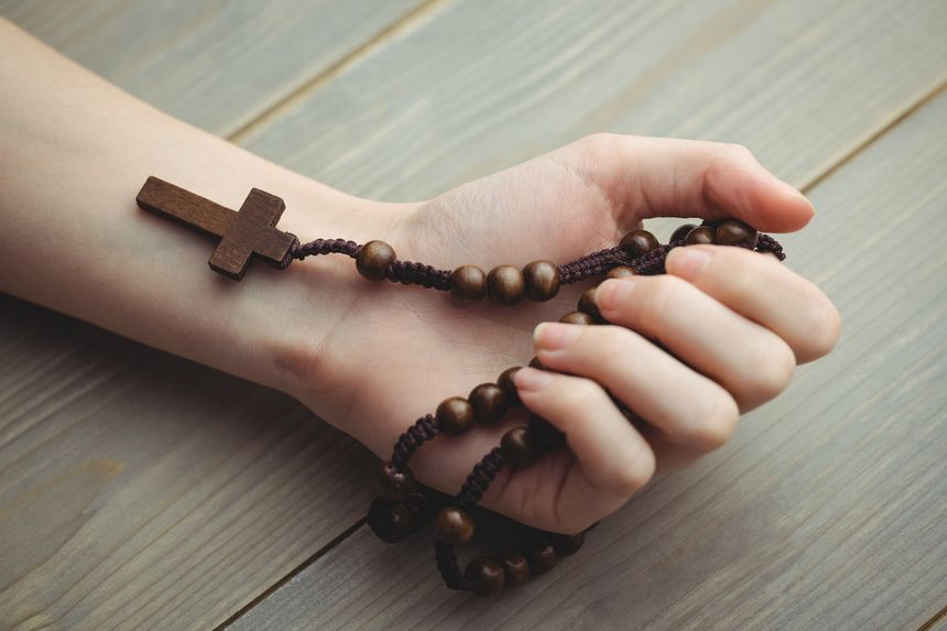 Woman holding wooden rosary beads on table