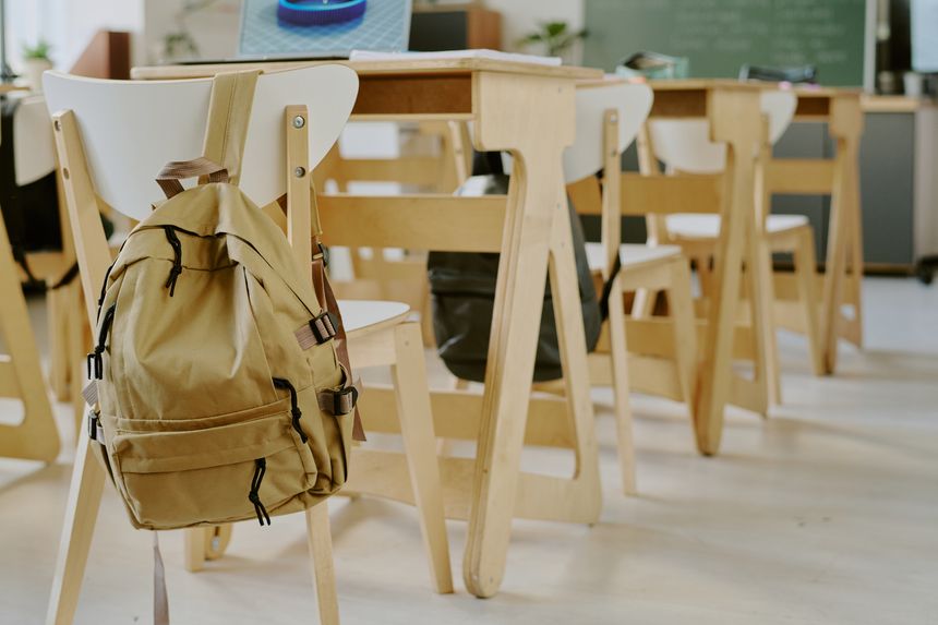 Interior of classroom showing empty chairs and desks, with backpack on back of one chair, suggesting absence of students or lesson in progress
