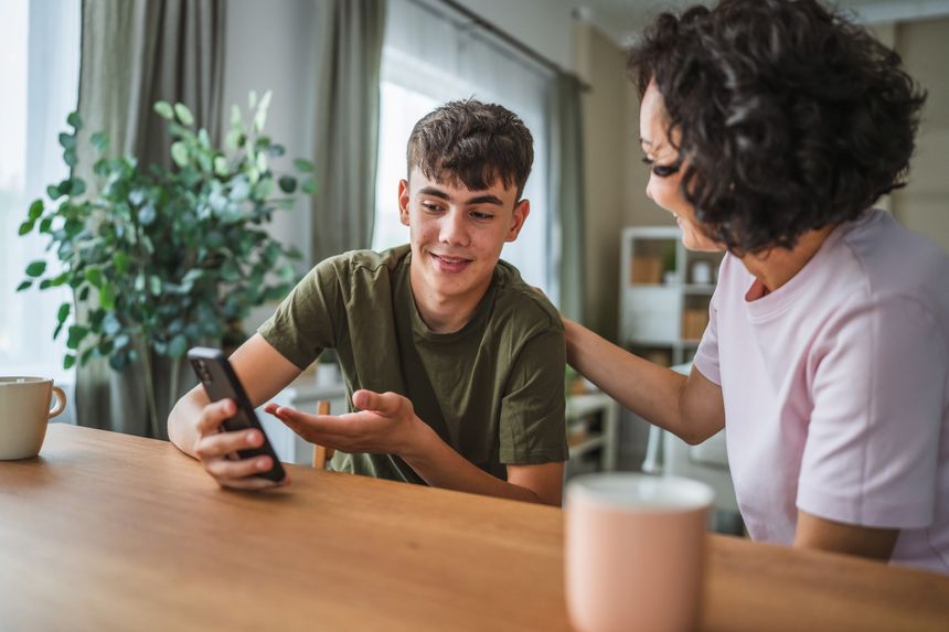 teenage boy share good news from mobile phone with his happy mother, celebrate together success at home