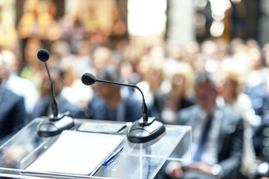 Microphones in focus at business conference, corporate presentation, workshop, coaching training, news conference, company meeting, public or political event. Public speaking concept.