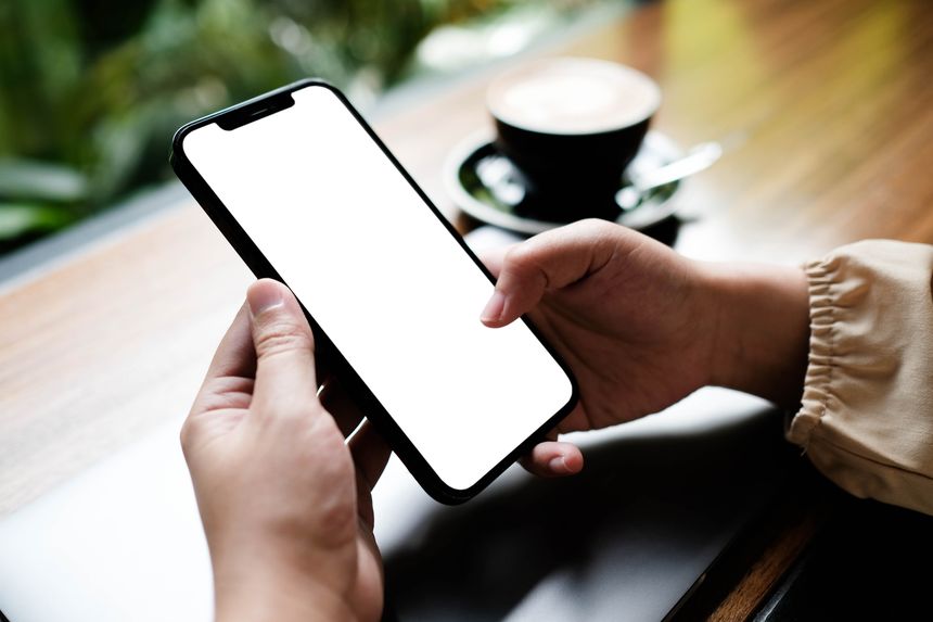 Woman sitting and holding blank screen mock up mobile phone with coffee cup at cafe.