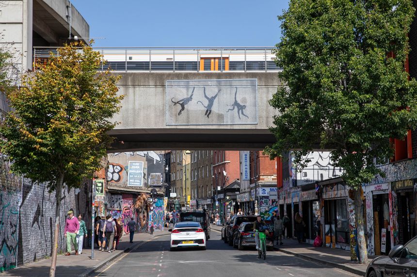 London, UK - August 23, 2024: Three monkeys swing from a bridge cross Brick Lane as depicted by artist Banksy