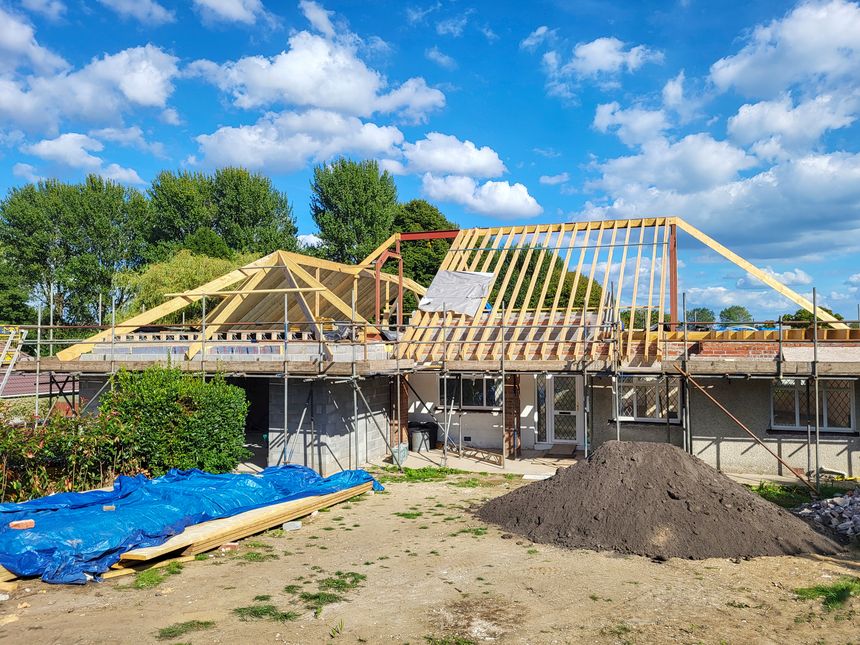 Swansea, UK: August 31, 2022: Single story self-build house during construction with scaffolding and exposed roof timbers.