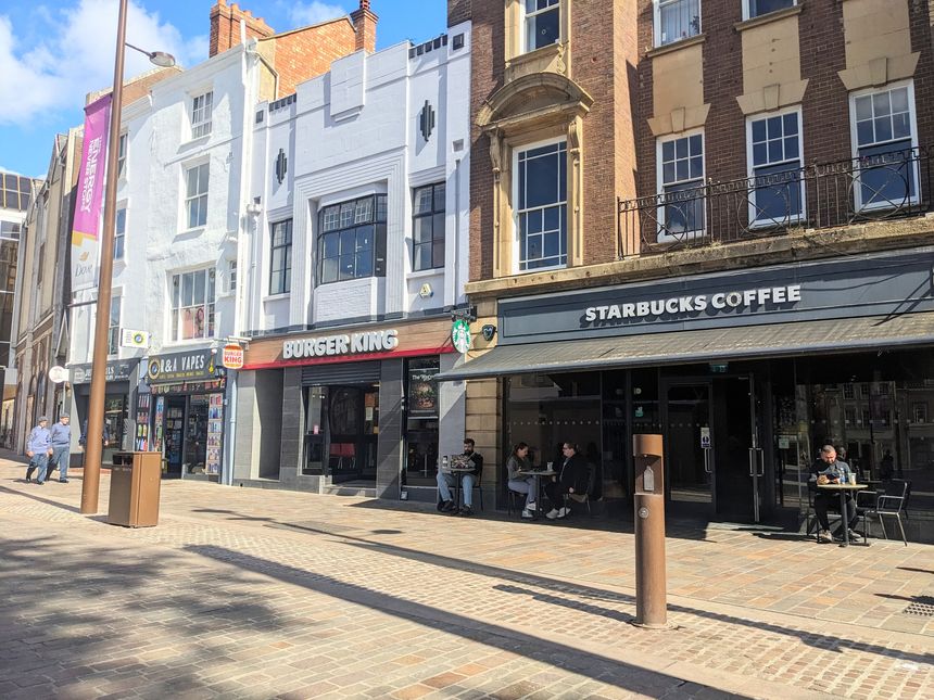 Northampton, UK - September 13 2025: People relax outside a Starbucks cafe on a sunlit pedestrian Market Square, with varied storefronts and classic English architecture under a blue sky in autumn