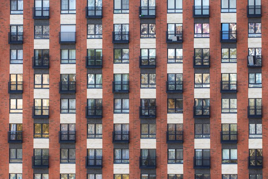 Facade of a tall brick apartment building with many windows and small balconies. Concept of: Urban density.