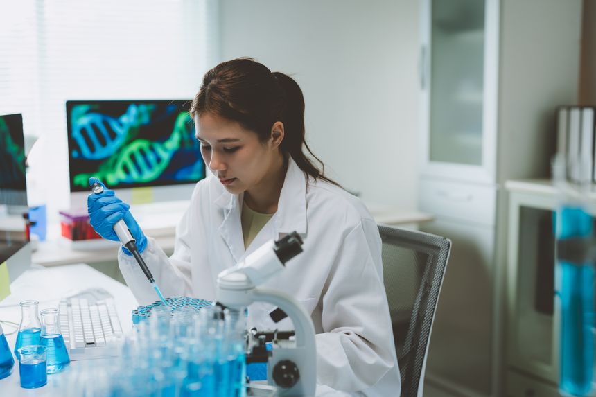 Young scientist performing experiment, pipetting liquid into vials with dna structure on computer screen. Researching genetics