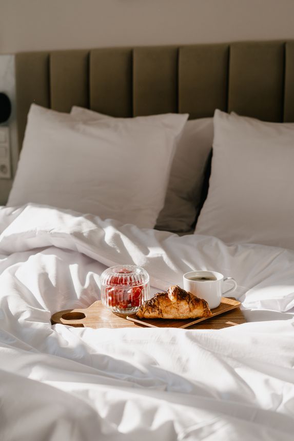 Room service. Bed and breakfast concepts. Relaxing morning with fresh linens and a tray holding a croissant, grapes and coffee cup in cozy bedroom. Weekend at home or while traveling, vertical shot
