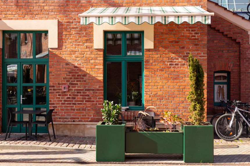 Street cafe with brick walls and canopy exterior design. Front view, sunny day. An outdoor cafe with tables, chairs. Lush green plants growing in pots near house.