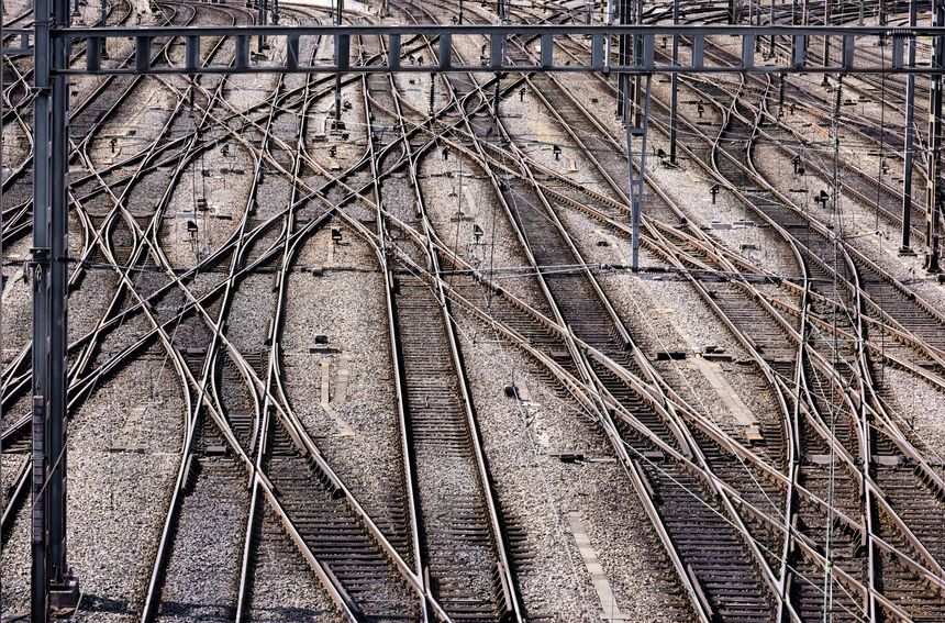 The railroad tracks in the photo form an impressive and complex layout that stretches across a vast area. The metal tracks run in various directions, creating an interwoven pattern that reflects the technical sophistication of the rail network. Gravel is visible between the tracks, serving as a stable base and supporting the tracks. In the background, additional tracks can be seen, complemented by electrical cables running across the facility, suggesting the potential electrification of the rail network. This industrial scene conveys a sense of dynamism and technology that is characteristic of modern railway infrastructure.