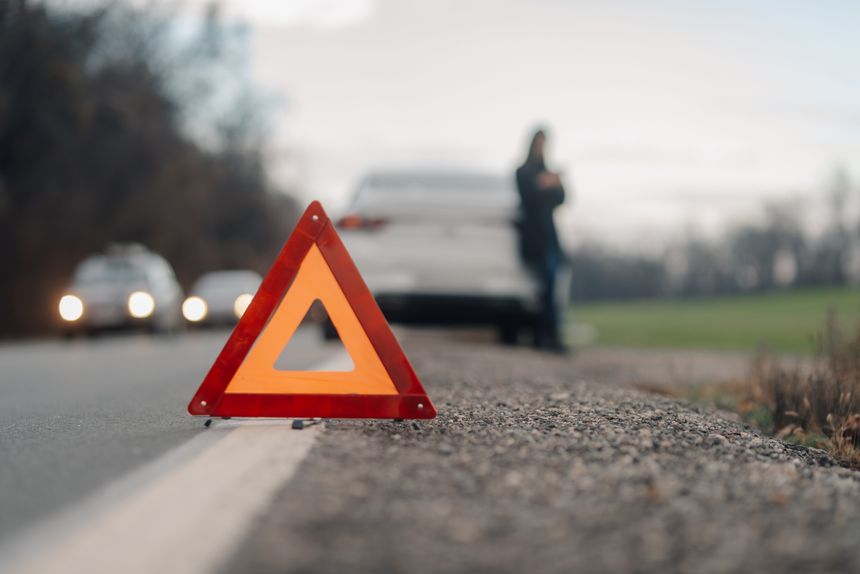 Driver waiting for assistance after placing warning triangle on a country road next to broken down car