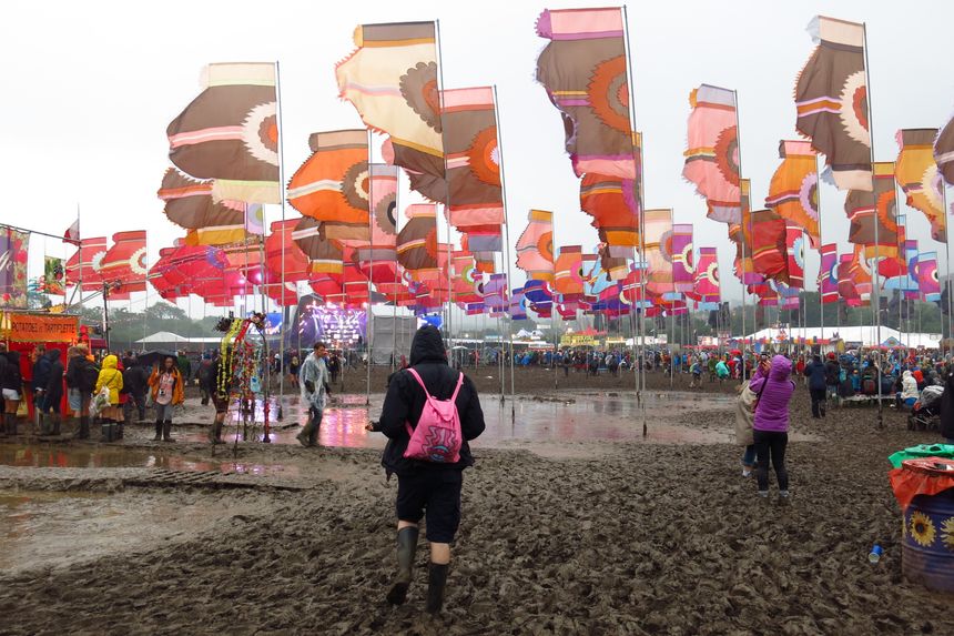 Glastonbury, United Kingdom - June 26, 2016: Deep mud and rain doesn’t deter revelers at Glastonbury Festival in Somerset, England. Music fans come prepared with rubber boots, ponchos and umbrellas.