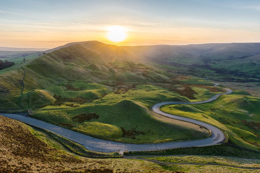 A long and winding rural road leading through lush green British countryside on a beautiful Summer evening. Taken from Mam Tor in the Peak District, UK.