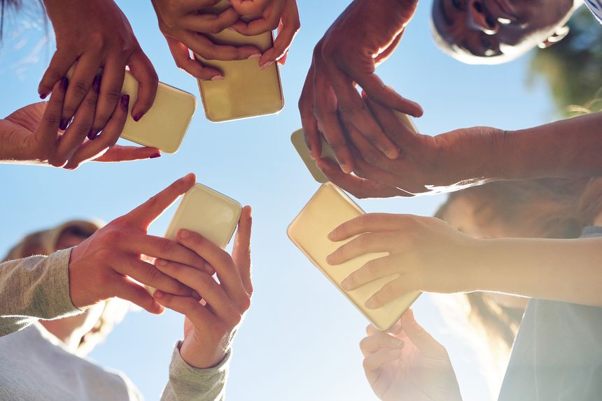 Cropped shot of a group of friends using their phones together outdoors