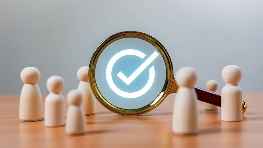 Selection and Quality Assurance in Recruitment. A magnifying glass focuses on a glowing checkmark surrounded by wooden figures, symbolizing selection, approval and business decision-making