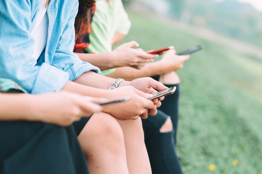 A cropped image of A group Asian friends are sitting using their smartphones and chatting in the park